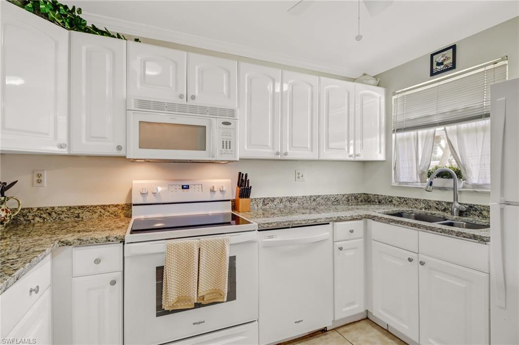 49 High Point Circle South, Unit 104 Naples, FL 34103 - Photo 14 of 30 a kitchen with white cabinets and white appliances