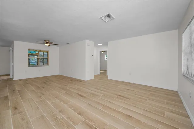 an empty room with wooden floor ceiling fan and windows
