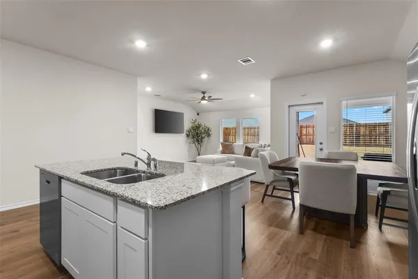 a kitchen island with granite countertop a sink and white cabinets with wooden floor