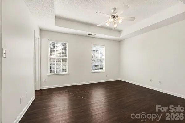 an empty room with wooden floor chandelier fan and windows