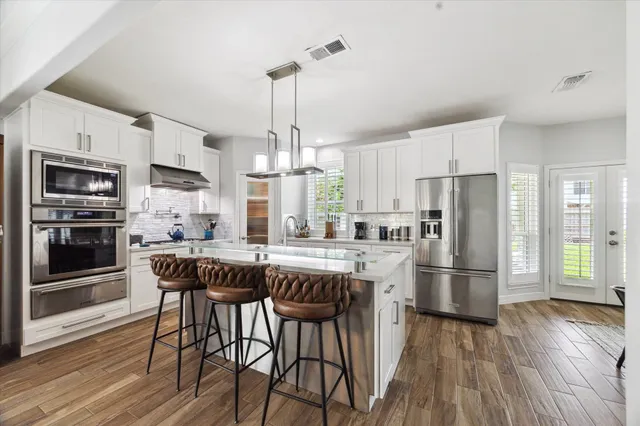 a kitchen with stainless steel appliances a dining table chairs refrigerator and microwave