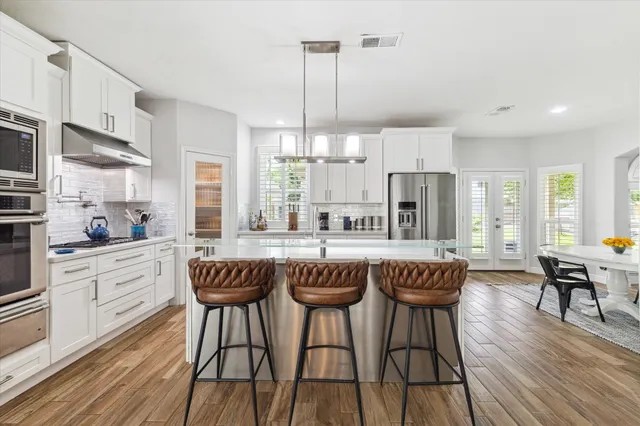 a kitchen with stainless steel appliances granite countertop a dining table chairs stove refrigerator and cabinets