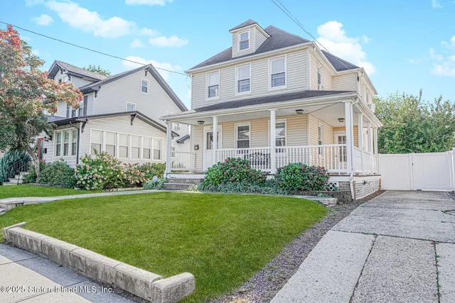 a view of a white house next to a yard with big trees