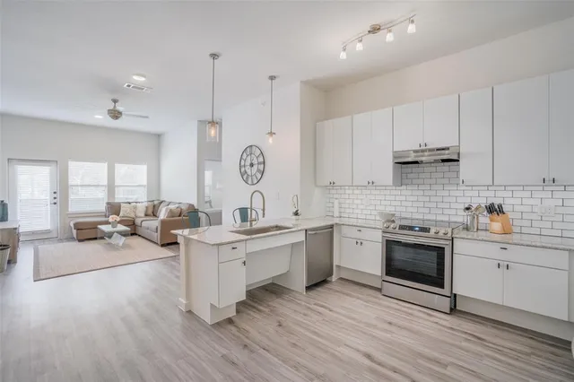 a large white kitchen with stainless steel appliances granite countertop a stove and a wooden floors