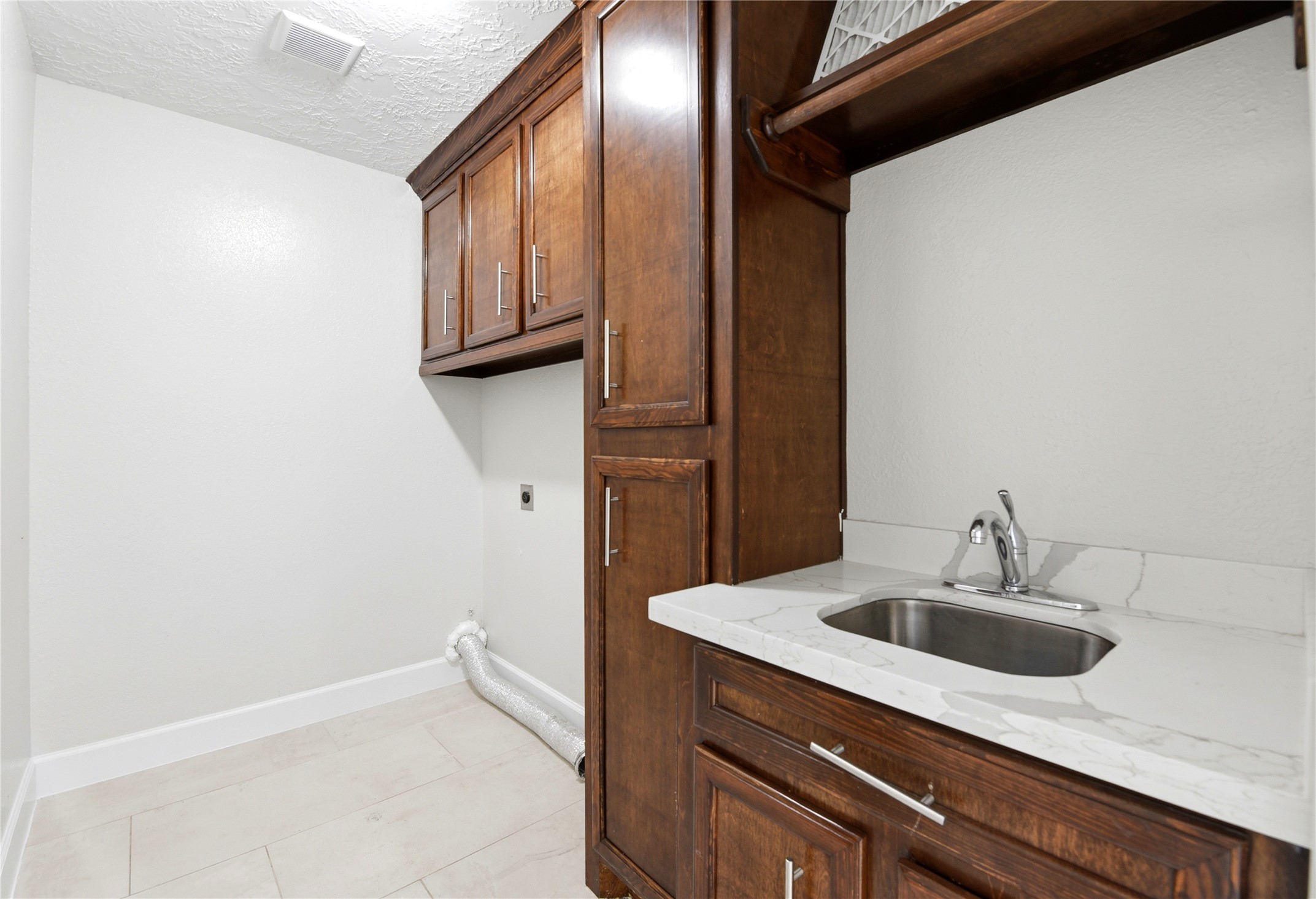 9403 Spaulding Street Houston, TX 77016 - Photo 28 of 50 This photo showcases a laundry room with elegant wooden cabinets, a marble countertop, and a small sink. The space is bright with tiled flooring, providing a clean and functional area for laundry tasks.