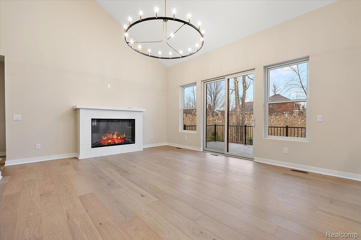 2044 Breckenridge Court Rochester, MI 48309 - Photo 14 of 33 Unfurnished living room with light wood-style floors, a glass covered fireplace, a chandelier, and high vaulted ceiling
