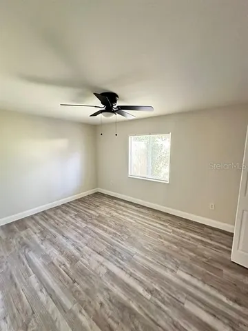 an empty room with wooden floor fan and windows