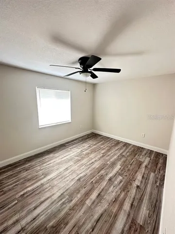 an empty room with wooden floor ceiling fan and windows
