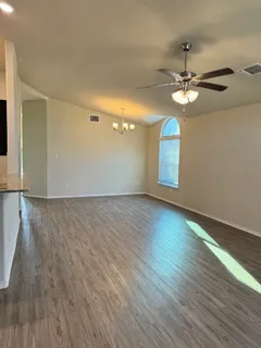an empty room with wooden floor chandelier fan and windows