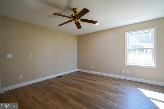 an empty room with wooden floor fan and windows