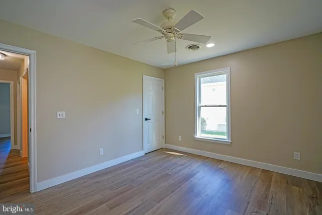 an empty room with wooden floor ceiling fan and windows