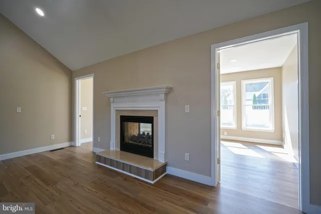 a view of an empty room with wooden floor fireplace and a window