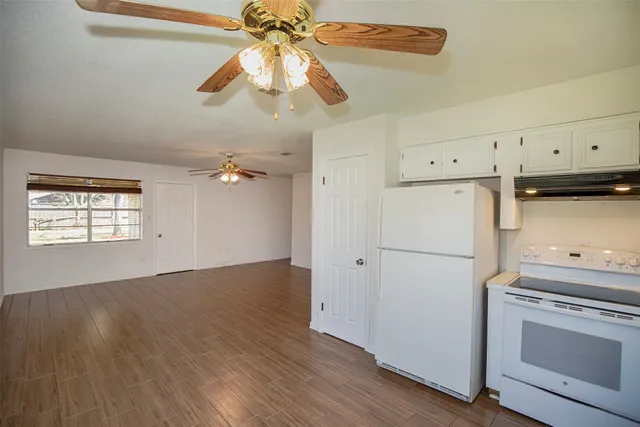 a kitchen with refrigerator a stove and white cabinets with wooden floor
