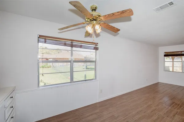 an empty room with wooden floor fan and windows