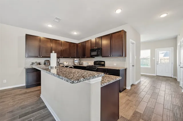 a kitchen with stainless steel appliances granite countertop a stove top oven a sink dishwasher a refrigerator and a oven with wooden floor