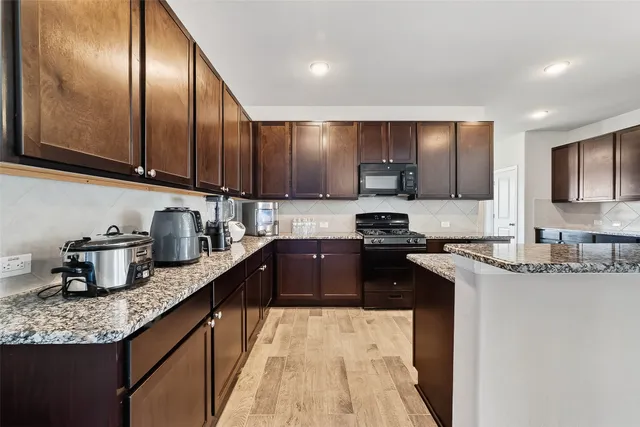 a kitchen with granite countertop stainless steel appliances a sink dishwasher a refrigerator a stove top oven and wooden cabinets