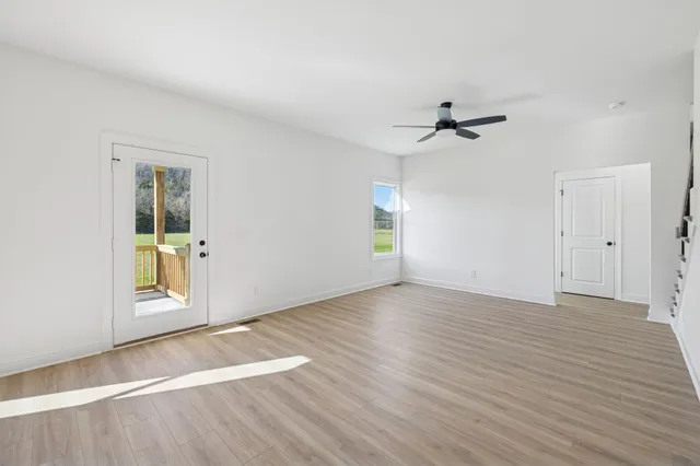 an empty room with wooden floor chandelier fan and windows