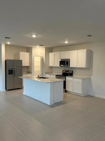 a large kitchen with stainless steel appliances granite countertop a stove a sink a refrigerator and white cabinets