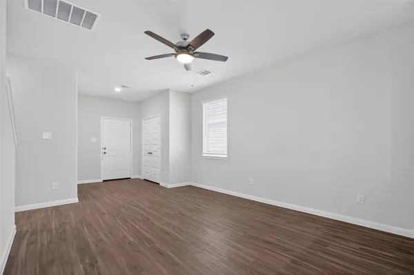 an empty room with wooden floor fan and windows