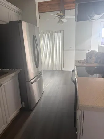 a view of a refrigerator in kitchen and an empty room with wooden floor