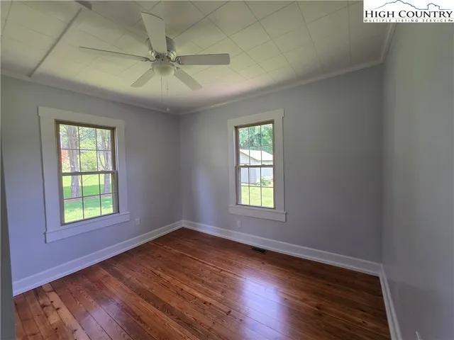 an empty room with wooden floor windows and fan