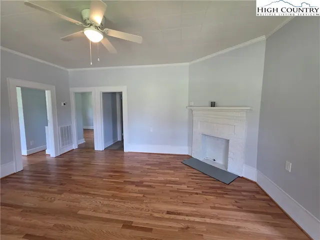 a view of an empty room with wooden floor and a ceiling fan