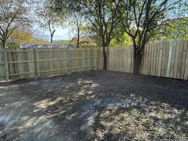 a view of a backyard with large trees and wooden fence