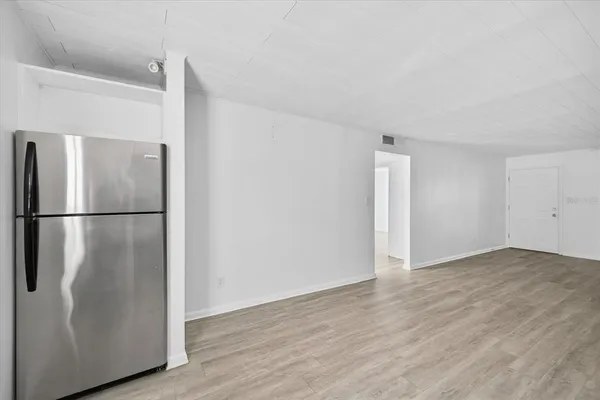 a view of an empty room with wooden floor and a kitchen