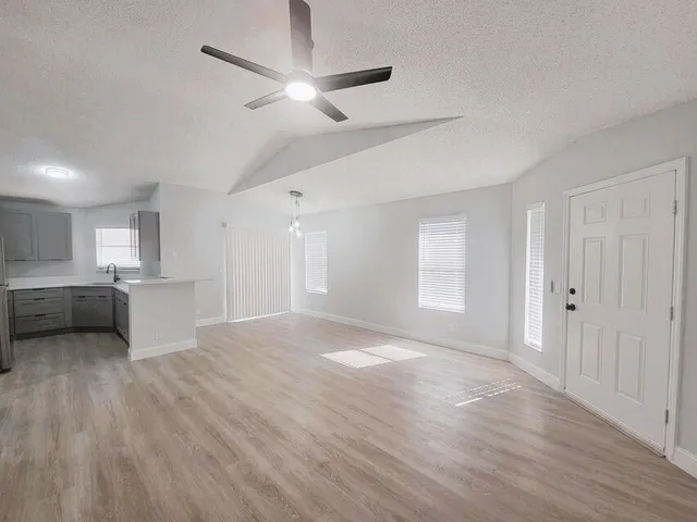 a view of an empty room with a window and a kitchen
