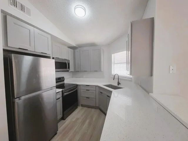 a kitchen with stainless steel appliances granite countertop a refrigerator a sink a stove and white cabinets