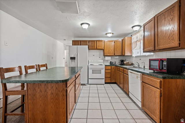 149 West 1600th Street South Mapleton, UT 84664 - Photo 11 of 44 Kitchen with dark countertops, a kitchen bar, wood finish cabinetry, white appliances, and a textured ceiling