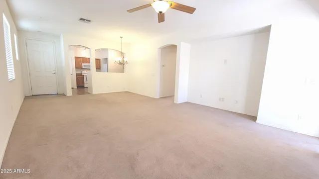 an empty room with chandelier fan and windows