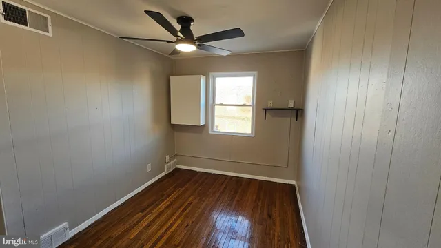 an empty room with wooden floor fan and windows