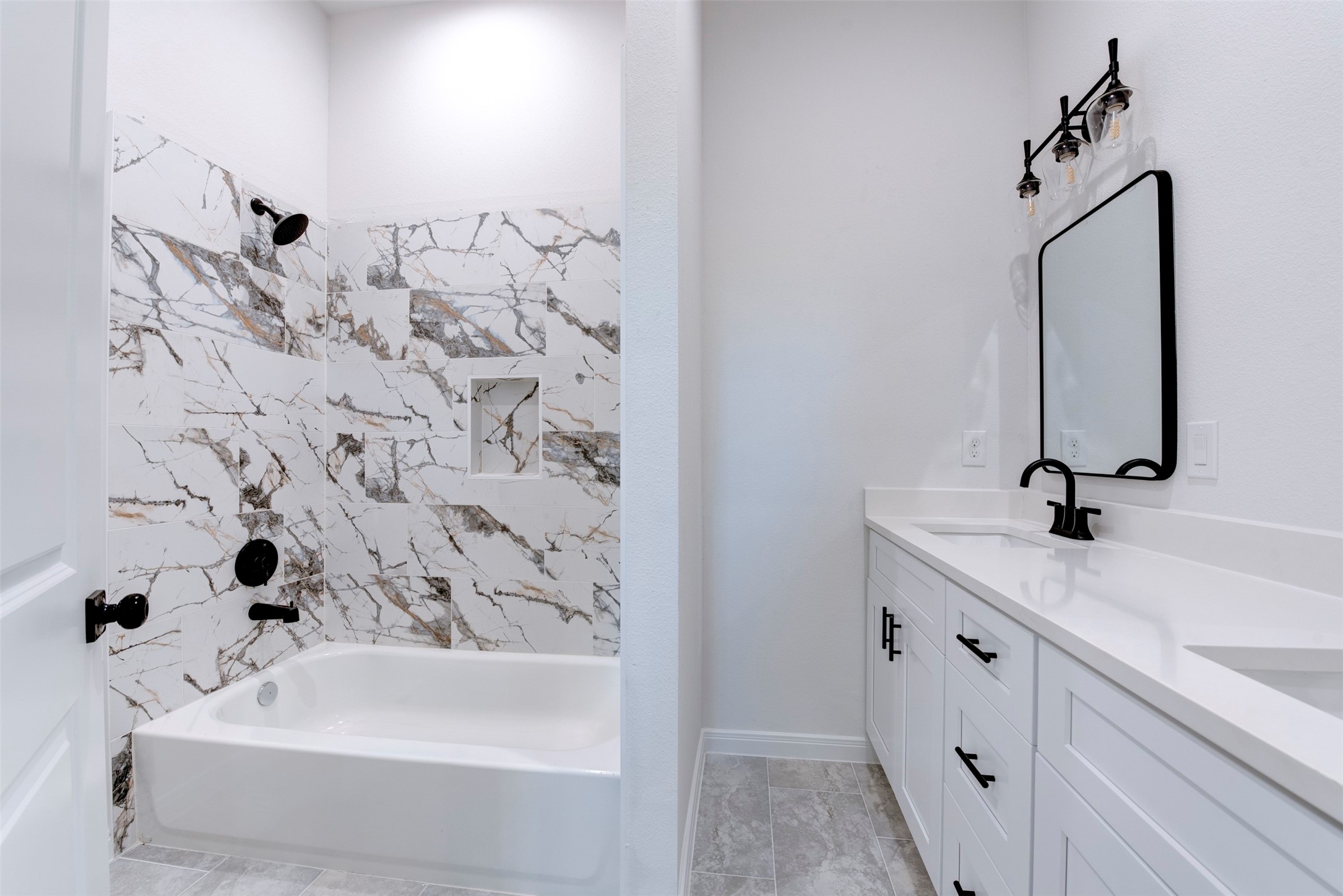 6809 Paris Street Houston, TX 77021 - Photo 21 of 37 Secondary bath featuring a striking marble-look tile surround with bold veining, paired with matte black shower fixtures. Double vanity with white shaker cabinetry, quartz countertop, and framed mirrors adds both style and functionality, finished with modern vanity lighting above.