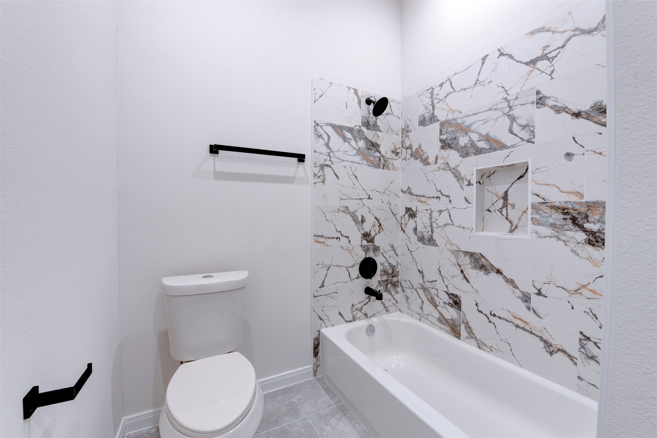 6809 Paris Street Houston, TX 77021 - Photo 22 of 37 Tub/shower combo finished with marble-look tile featuring bold veining, paired with matte black fixtures for a clean, modern contrast. Built-in niche adds practical storage, while light tile flooring keeps the space bright and cohesive
