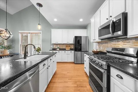 a kitchen with stainless steel appliances granite countertop a sink a stove top oven a refrigerator cabinets and a kitchen island