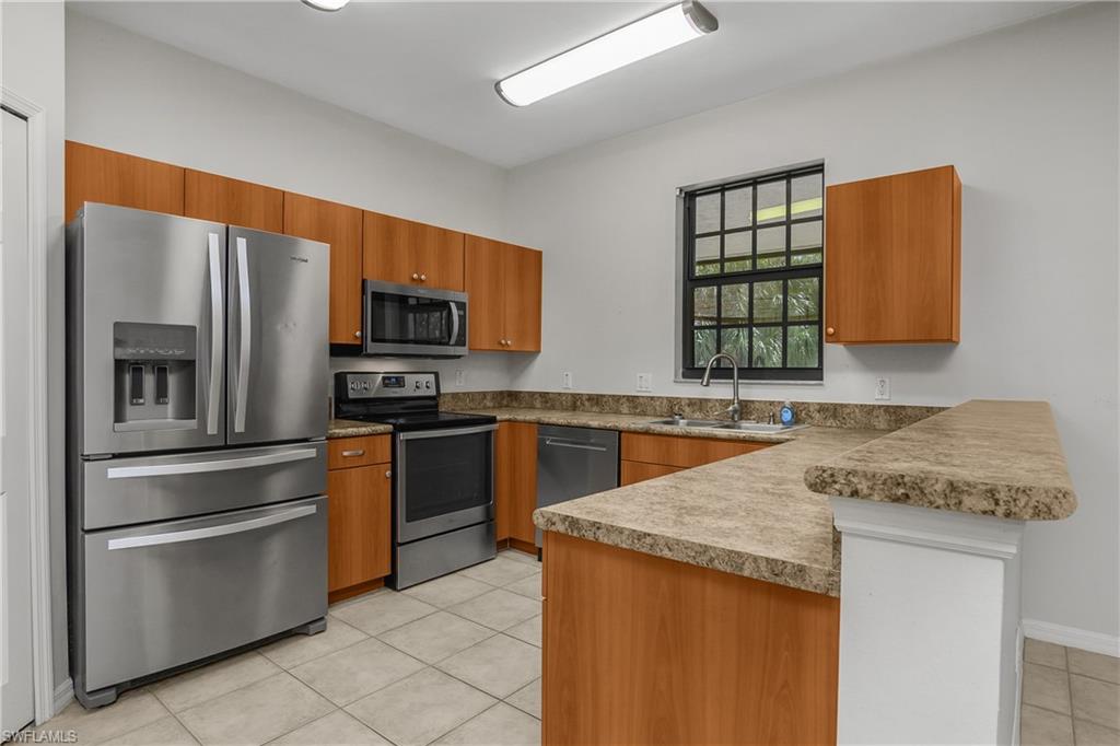 15186 Summit Pl Circle Naples, FL 34119 - Photo 21 of 37 Kitchen featuring stainless steel appliances, a peninsula, wood finish cabinetry, light tile patterned floors, and a kitchen bar