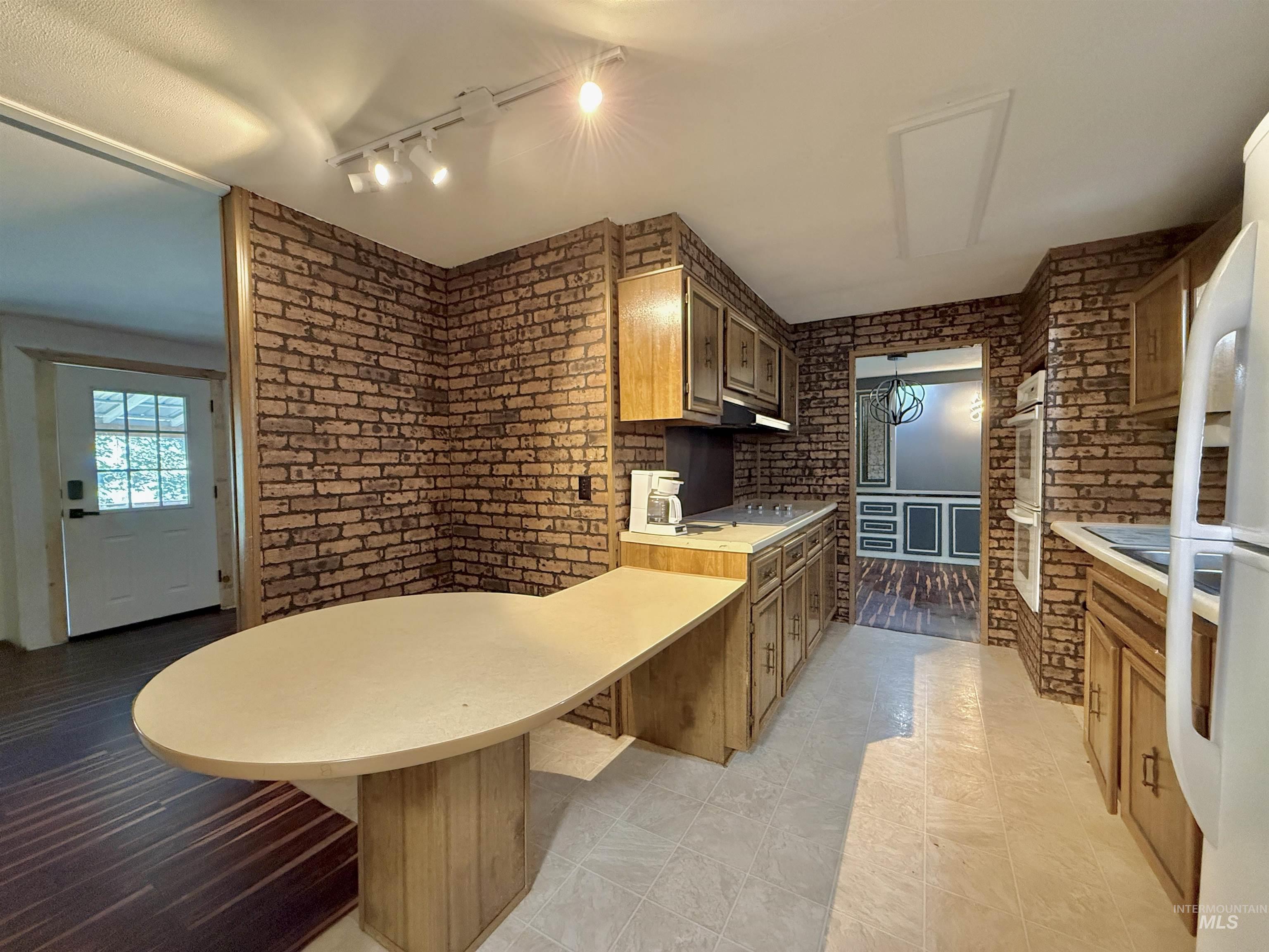 191 Battle Ridge Road Kooskia, ID 83539 - Photo 12 of 35 Kitchen featuring light countertops, a peninsula, brick wall, white appliances, and brown cabinetry