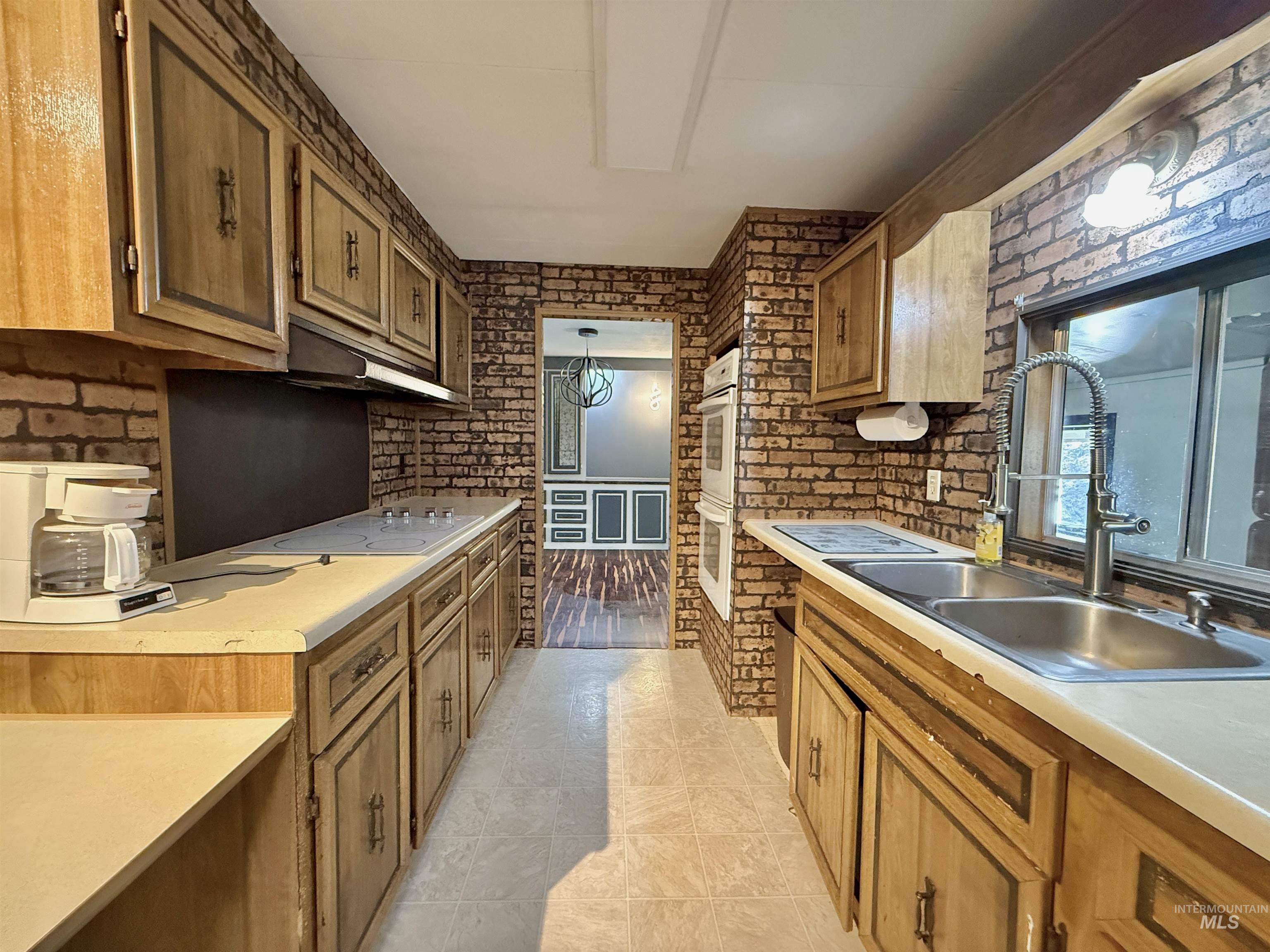 191 Battle Ridge Road Kooskia, ID 83539 - Photo 13 of 35 Kitchen featuring brick wall, light countertops, brown cabinetry, under cabinet range hood, and light tile patterned floors