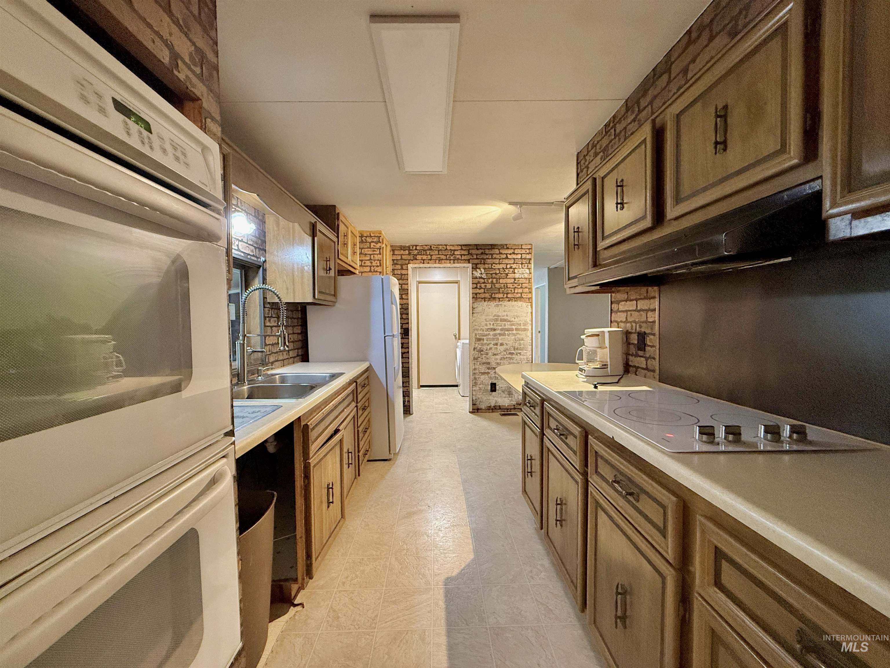 191 Battle Ridge Road Kooskia, ID 83539 - Photo 14 of 35 Kitchen featuring white appliances, brick wall, light countertops, brown cabinetry, and under cabinet range hood