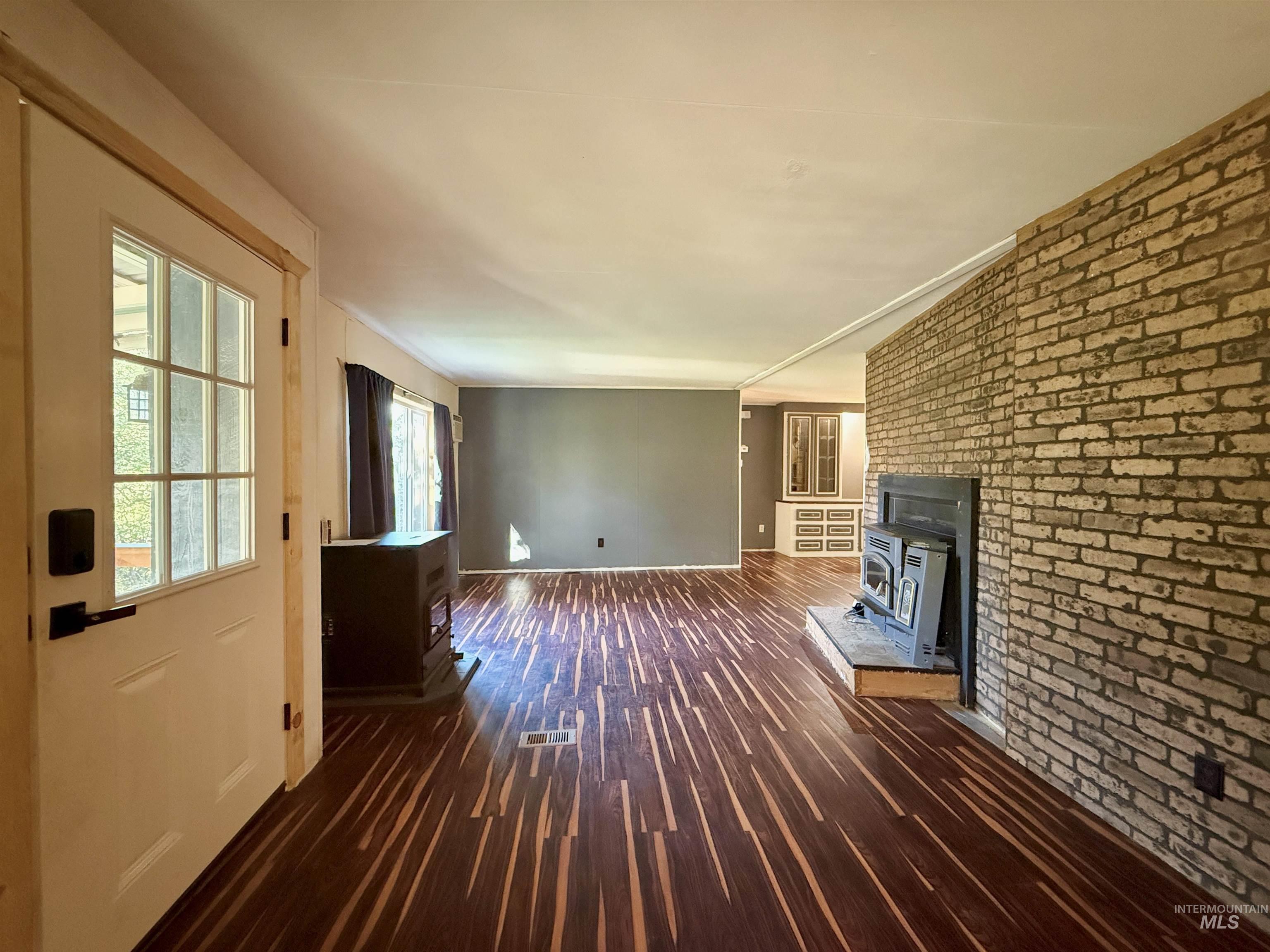 191 Battle Ridge Road Kooskia, ID 83539 - Photo 7 of 35 Unfurnished living room with a wood stove, brick wall, dark wood-style floors, and crown molding