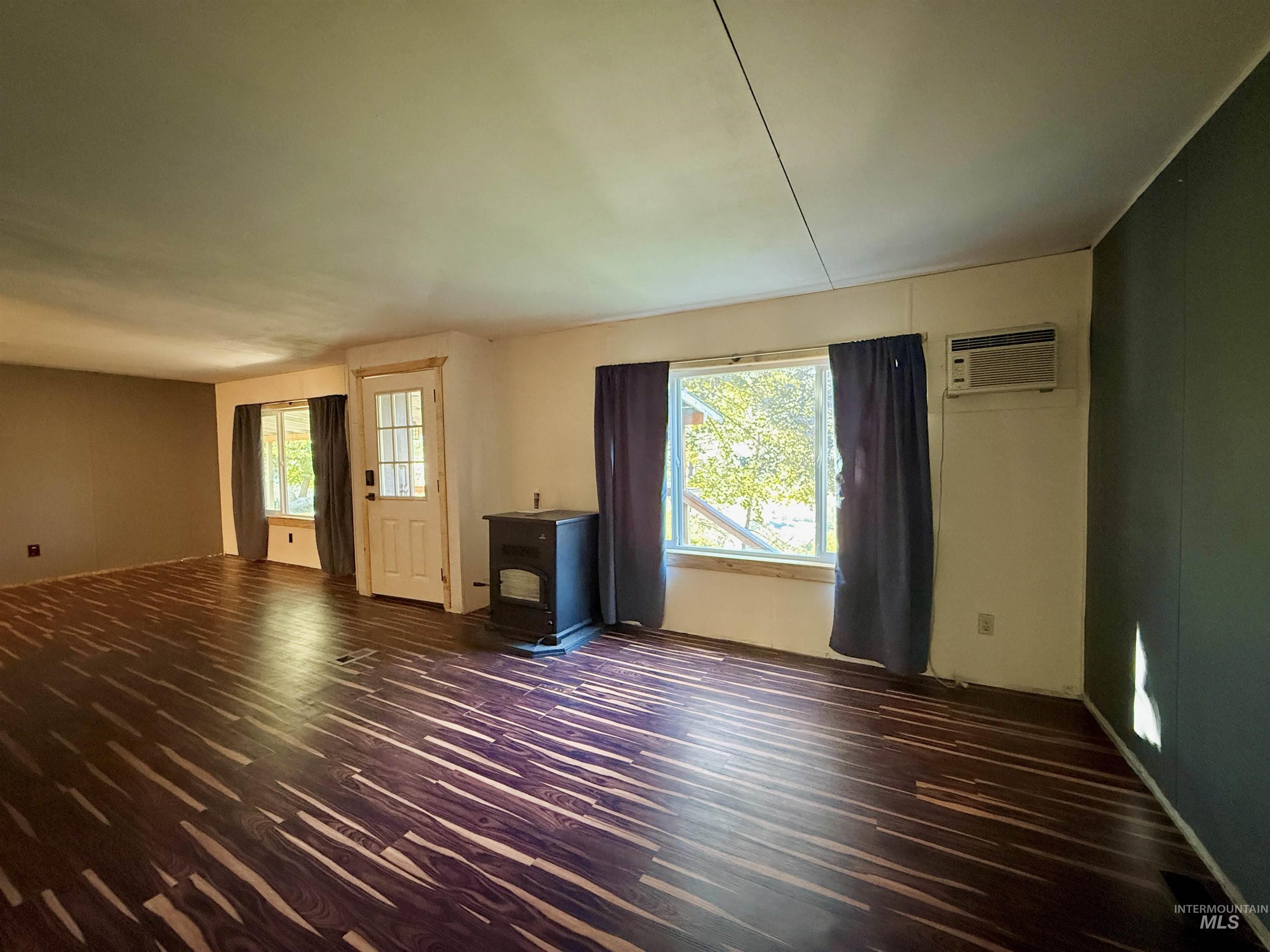 191 Battle Ridge Road Kooskia, ID 83539 - Photo 8 of 35 Unfurnished living room featuring dark wood-style floors, a wood stove, and a wall mounted air conditioner