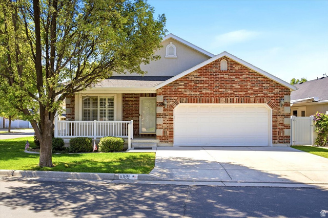 1089 West 2325th Street North Layton, UT 84041 - Photo 1 of 40 Brick and stucco exterior featuring a two-car garage, covered porch with white railing, and a manicured lawn