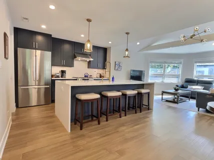 a kitchen with stainless steel appliances granite countertop a refrigerator a kitchen island a stove a sink a dining table and chairs with wooden floor