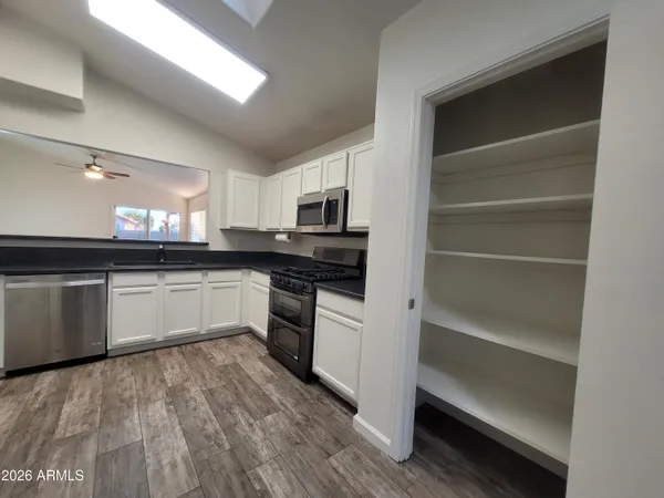 a white kitchen with granite countertop a stove top oven a sink and dishwasher with wooden floor