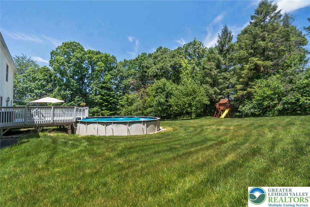 9461 Red Road Kempton, PA 19529 - Photo 43 of 55 A spacious yard offers an above-ground pool, expansive deck, and shaded play area amidst lush greenery.