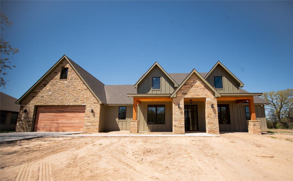 View of front of home with stone siding, roof with shingles, an attached garage, board and batten siding, and dirt driveway