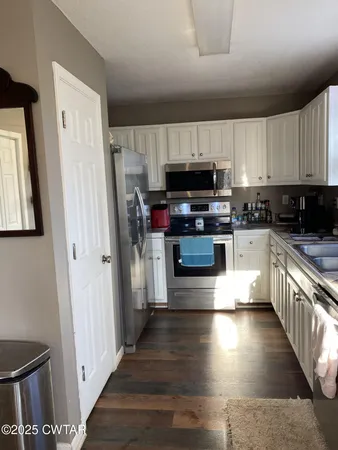 a kitchen with stainless steel appliances wooden floors and a view of living room