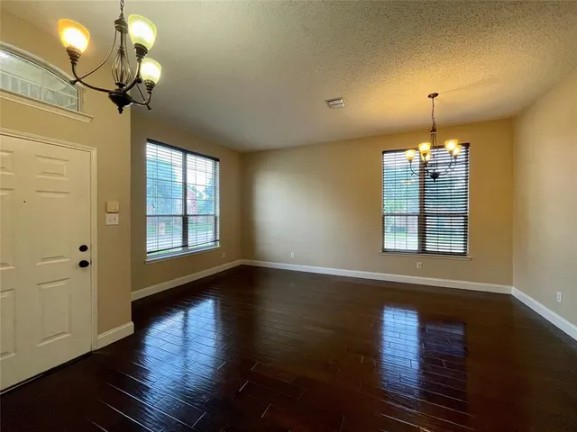 an empty room with wooden floor chandelier and windows