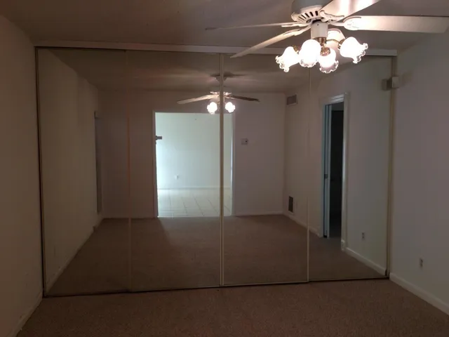 an empty room with a chandelier fan and wooden floor
